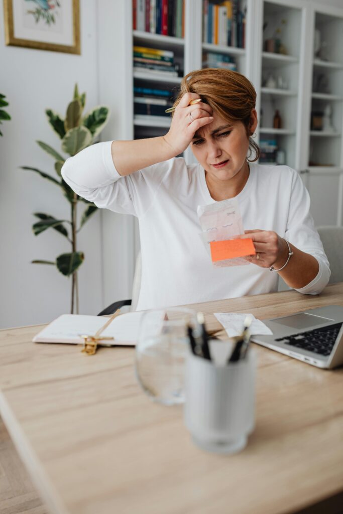 A businesswoman in an office looks frustrated while reviewing bills and finances with a laptop, displaying anxiety.