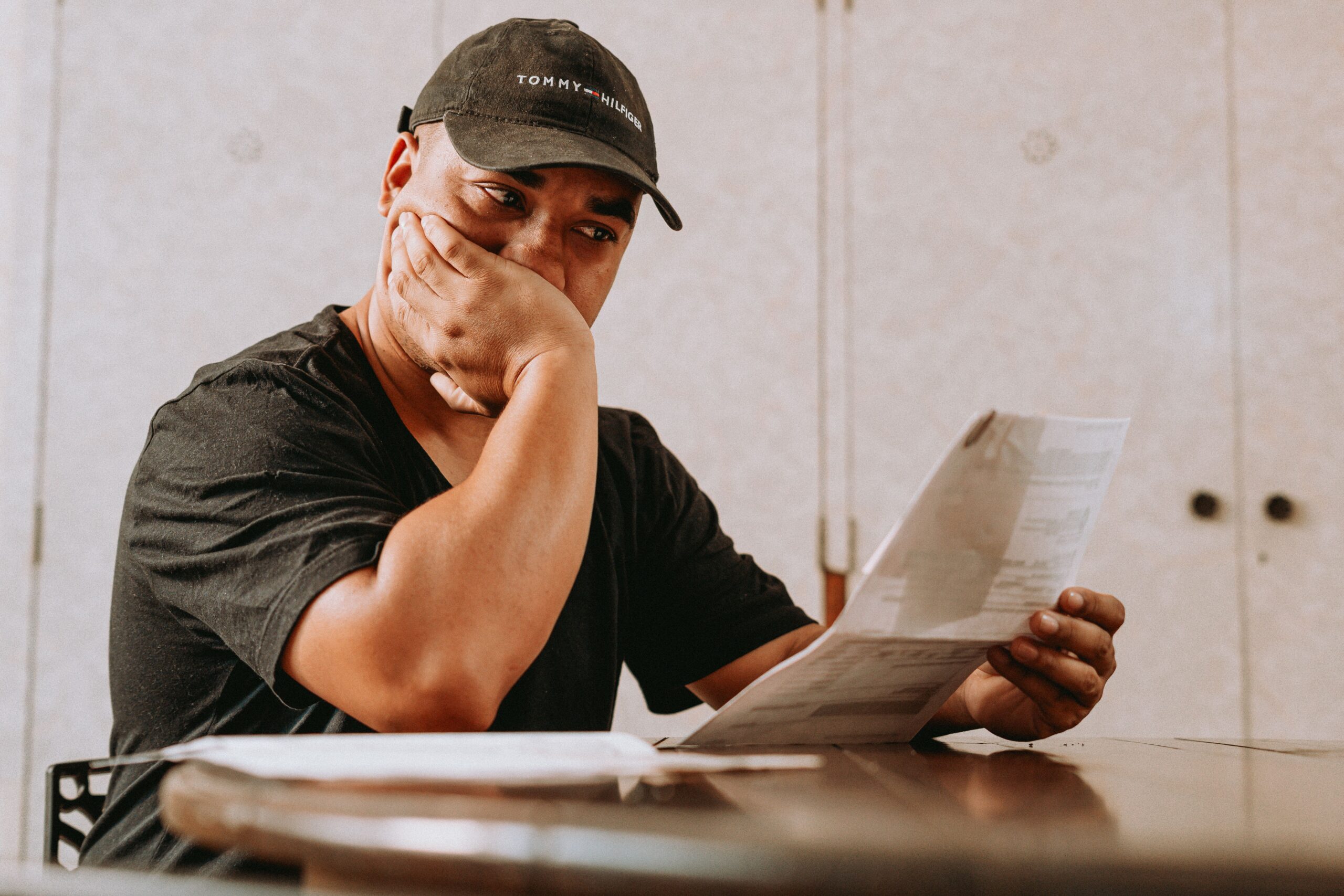 A man sits indoors, deeply focused on reviewing paperwork, expressing concern and contemplation.