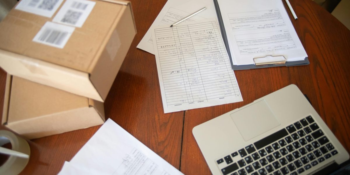 Flat lay of a workspace with laptop, documents, and cardboard boxes for e-commerce operations.